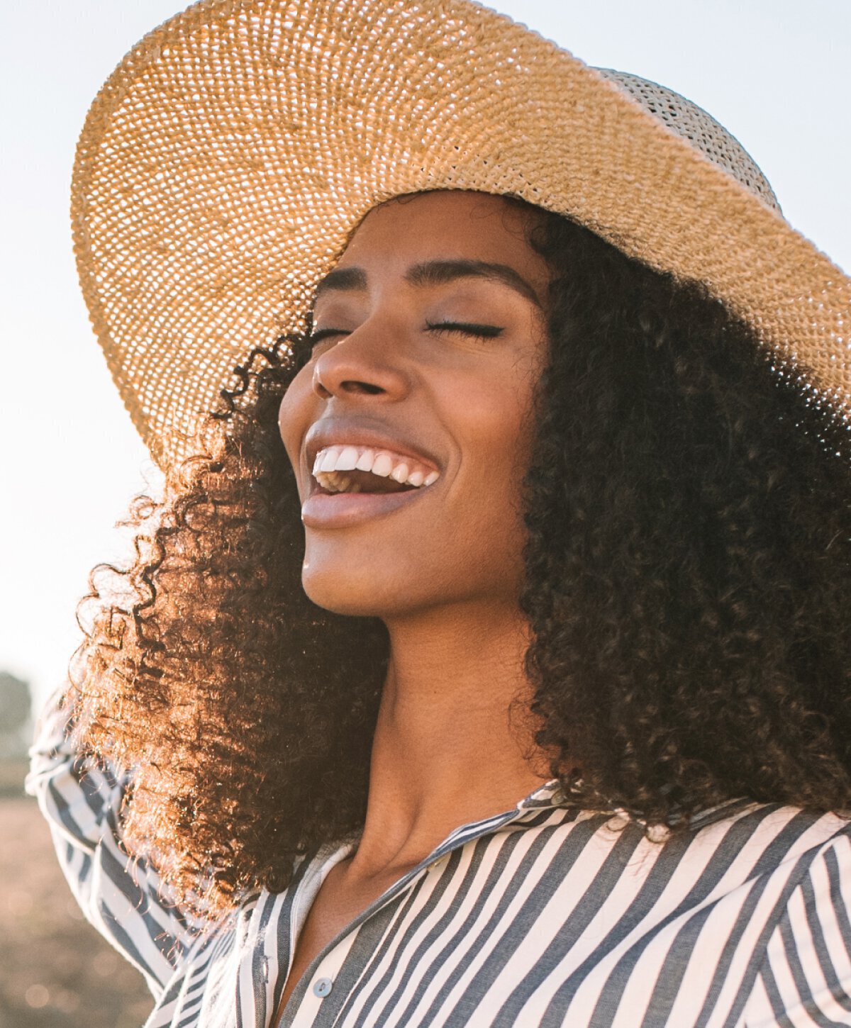 houston botox model with curly black hair smiling in sun hat
